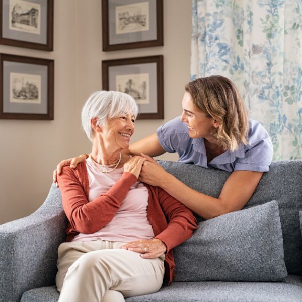 senior woman on couch in apartment receiving encouragement from female medical professional