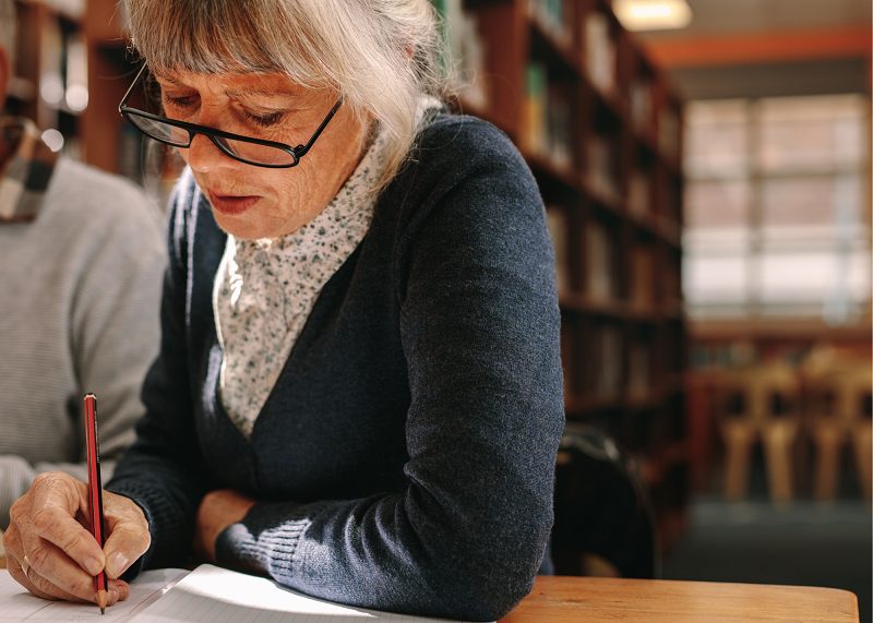 senior woman in library writing in notebook