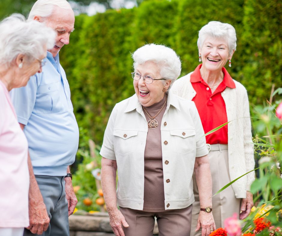 3 older women and an older gentleman laughing in garden setting