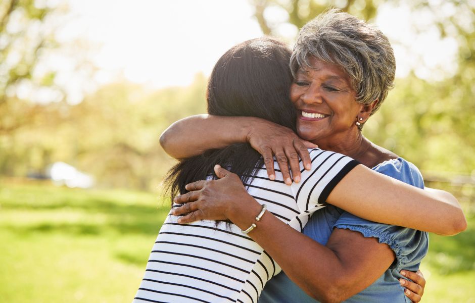 a young black woman hugging a smiling,senior black woman in an outdoor setting