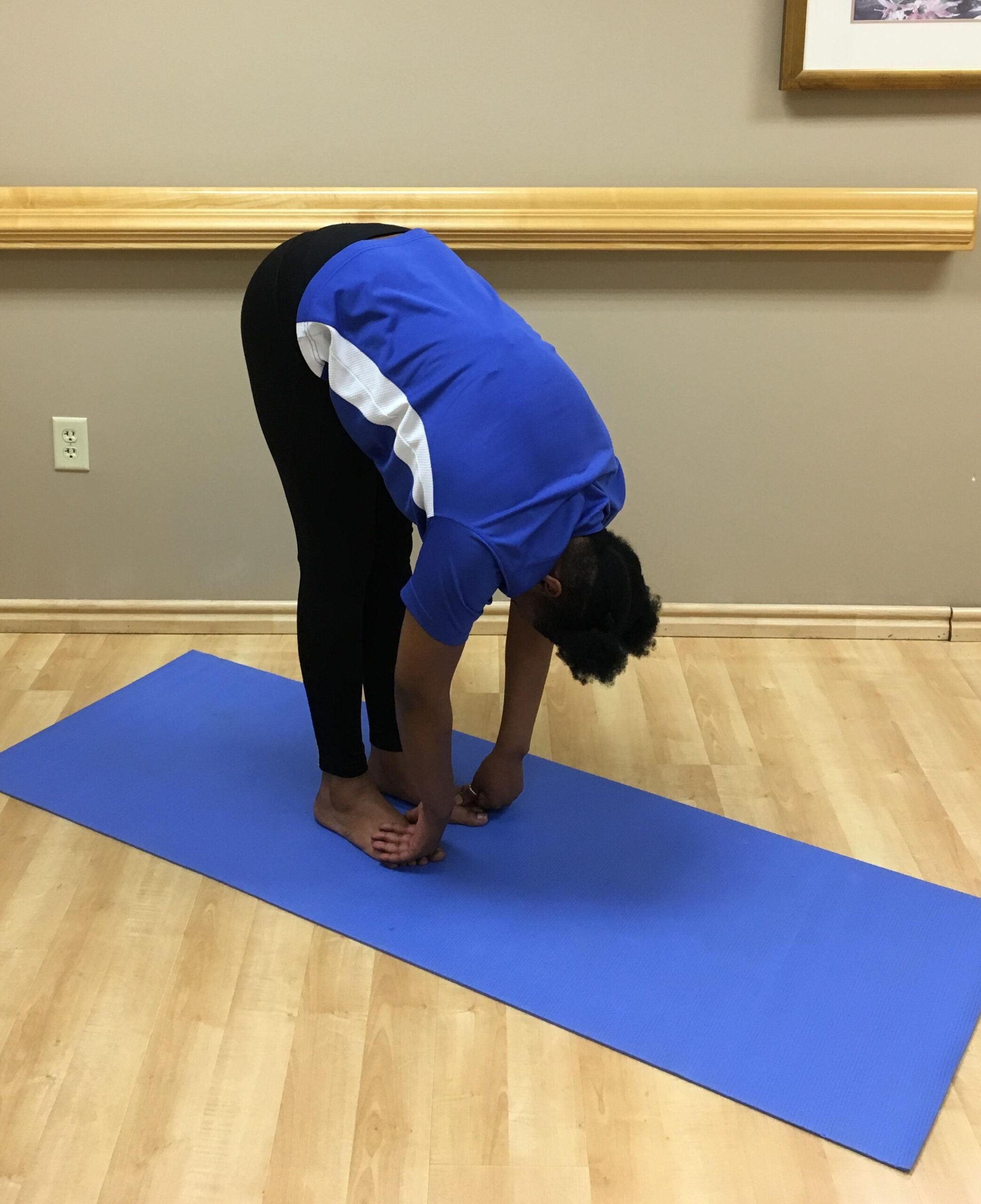 woman standing on yoga mat bend over nearly touching her toes