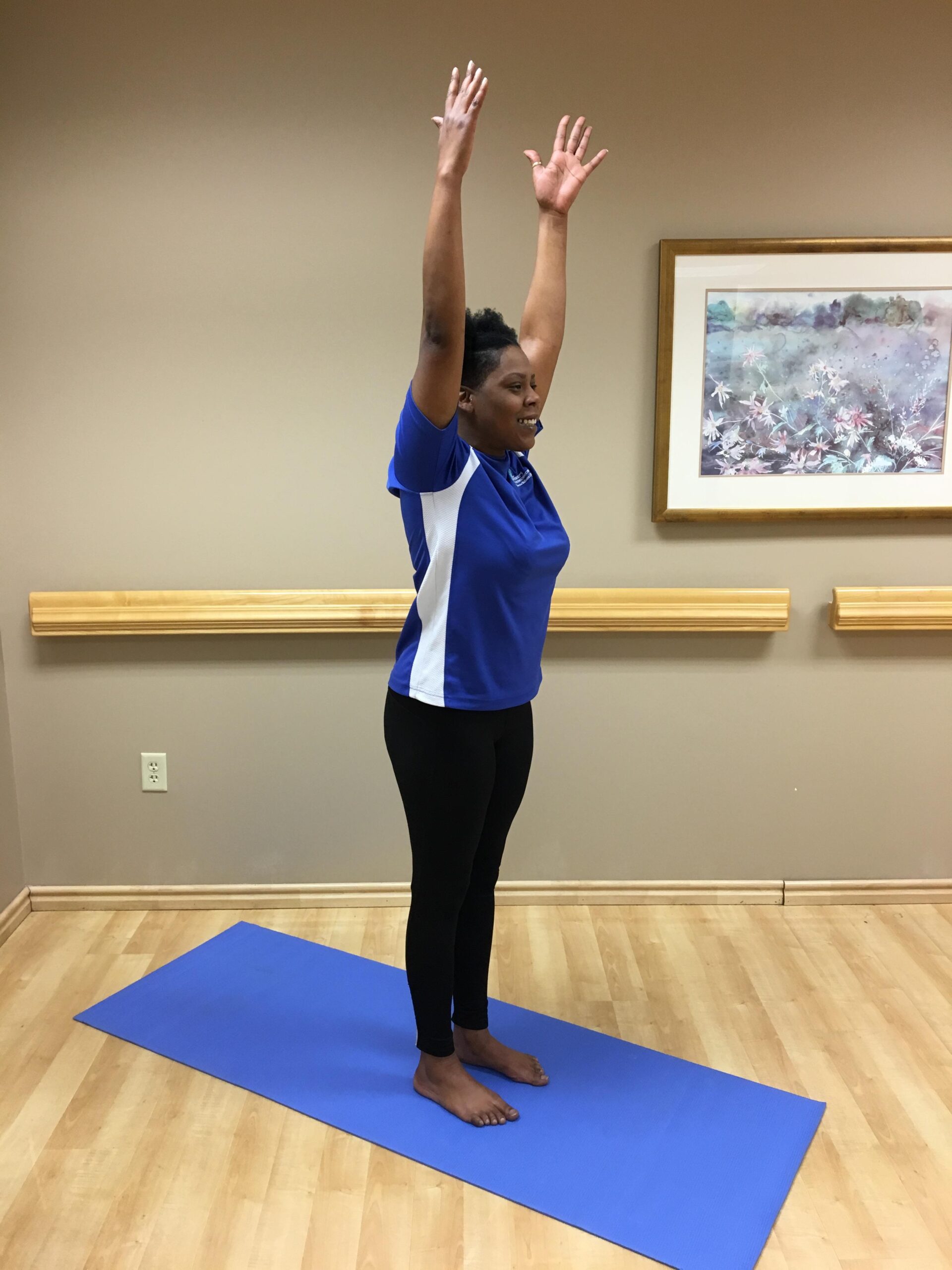 woman on yoga mat standing with arms straight up