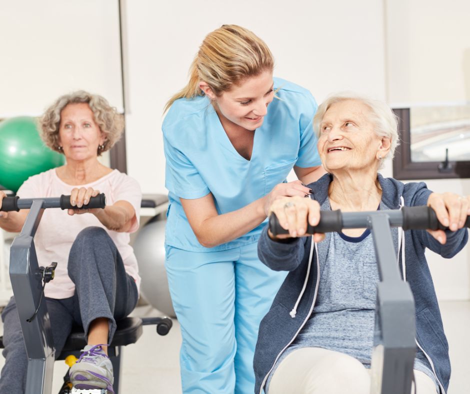 two senior women working out on recumbent exercise bike with physical therapist assisting