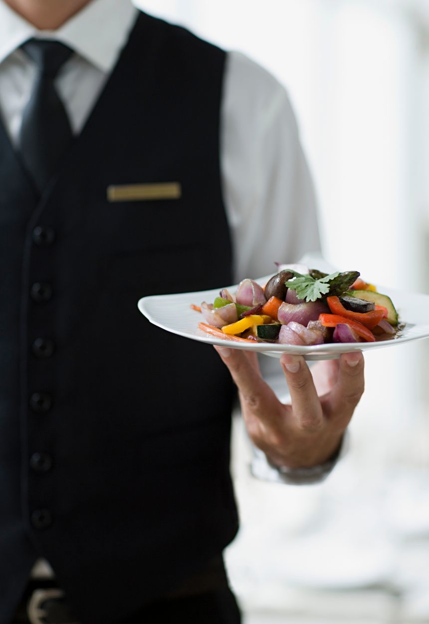 male server holds plate of colorful vegetables