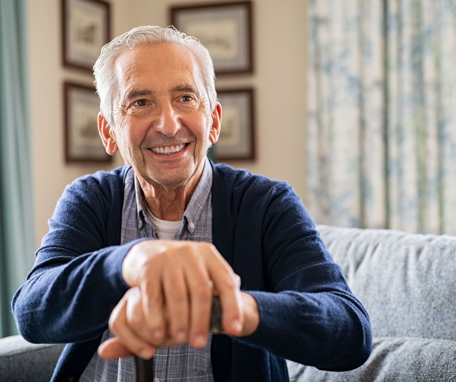 senior man sitting on couch with hands on top of cane