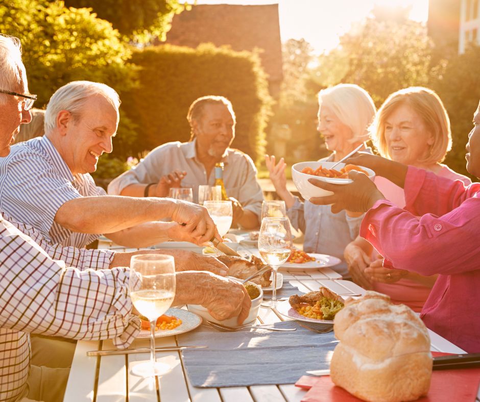 group of seniors enjoying wine and a meal on picnic table outside in bring sunlight