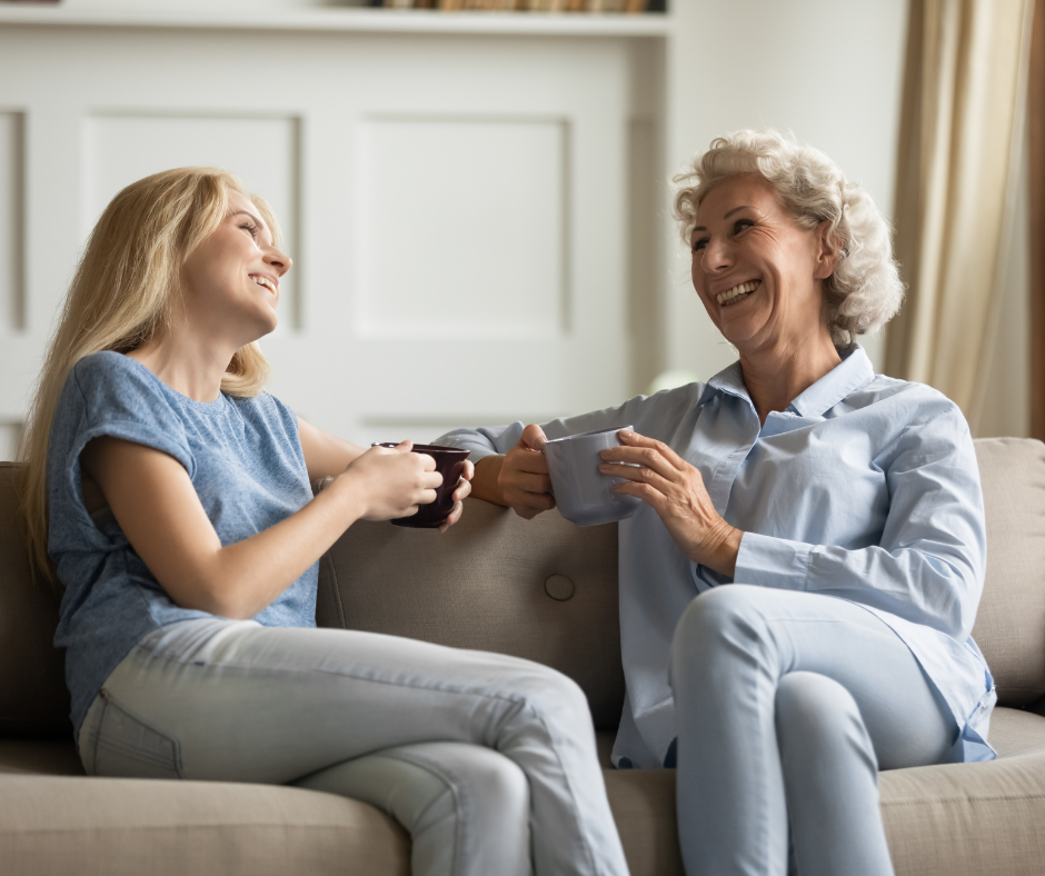 mother and daughter smiling at each other while sitting on the couch having coffee