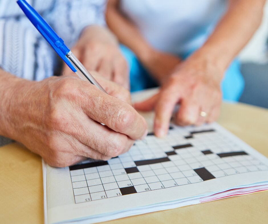 Close-up of an older adult filling in a crossword puzzle with a blue pen.