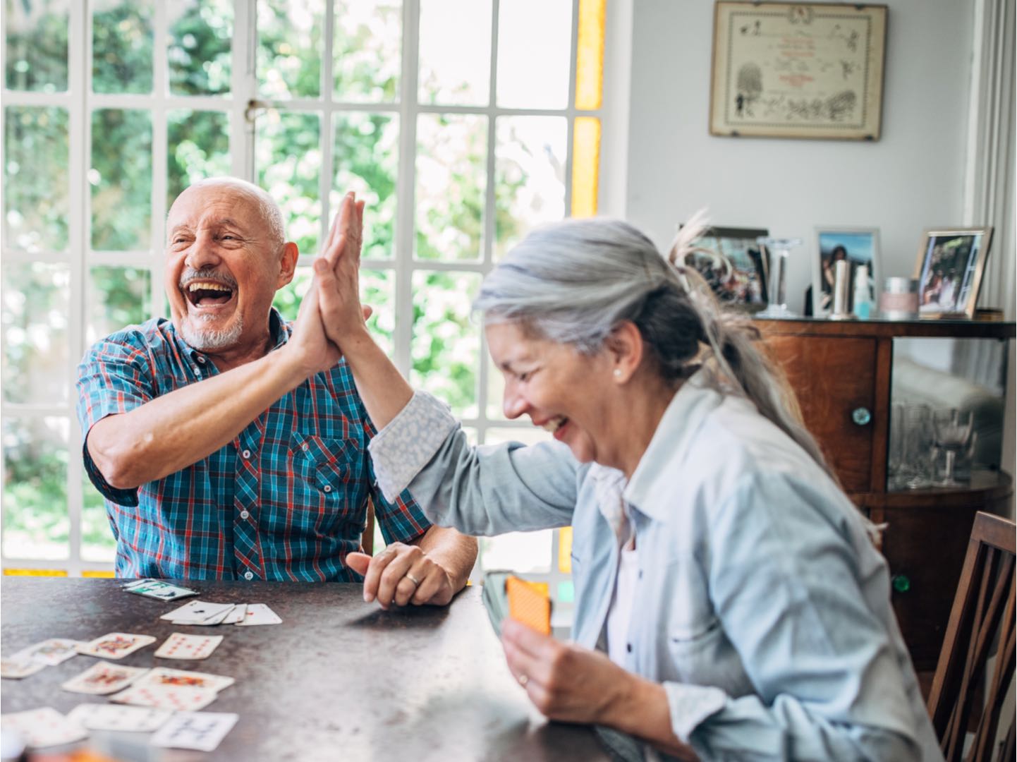 senior couple giving high five while laughing and playing cards in a dining room