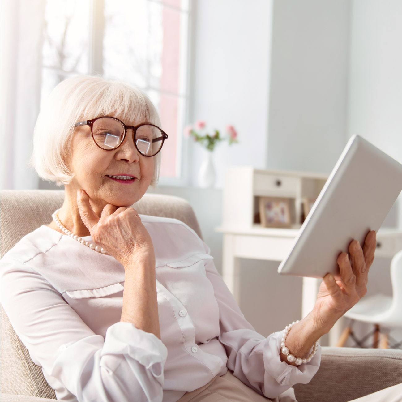 Senior woman sitting in senior living apartment reading off an ipad