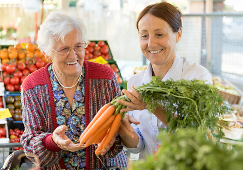 senior woman with female caregiver at a farmers market buying carrots
