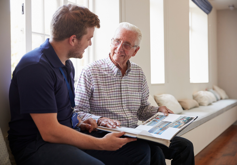 senior man with dementia looking at photo album with caregiver