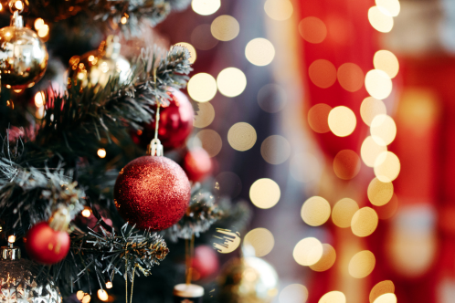 An image of a Christmas tree with red ornaments and blurred lights in the background