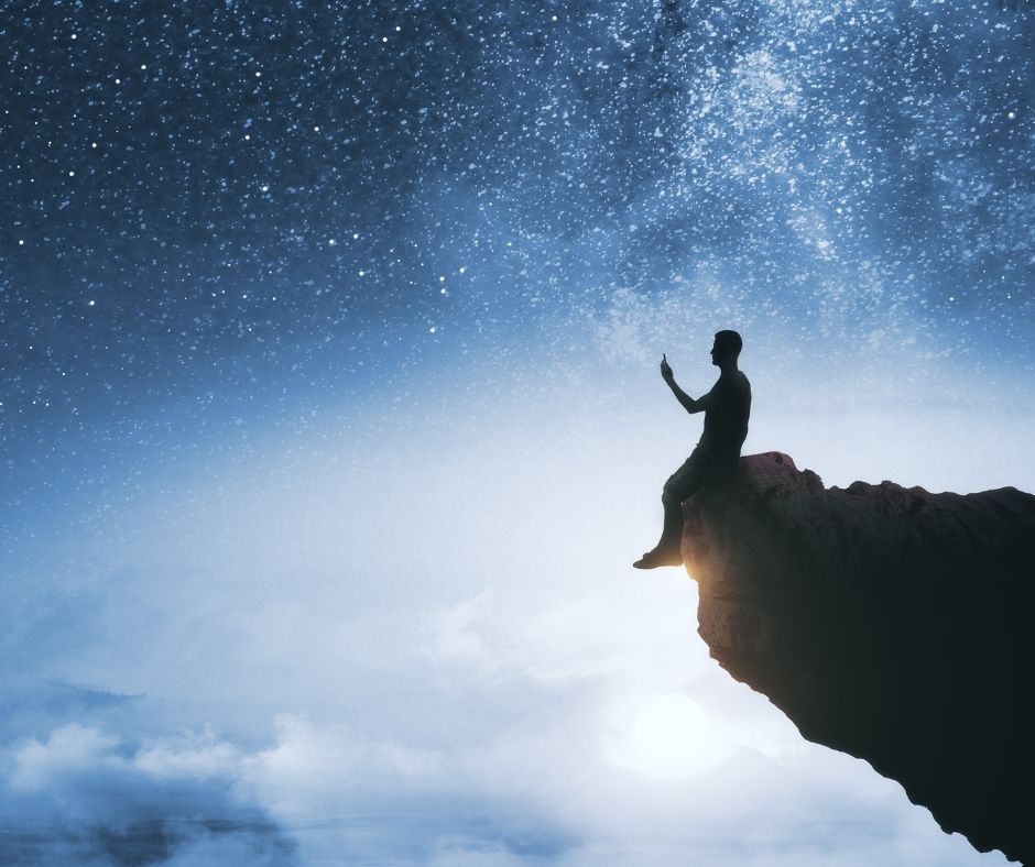 man on cliff with starry sky in background