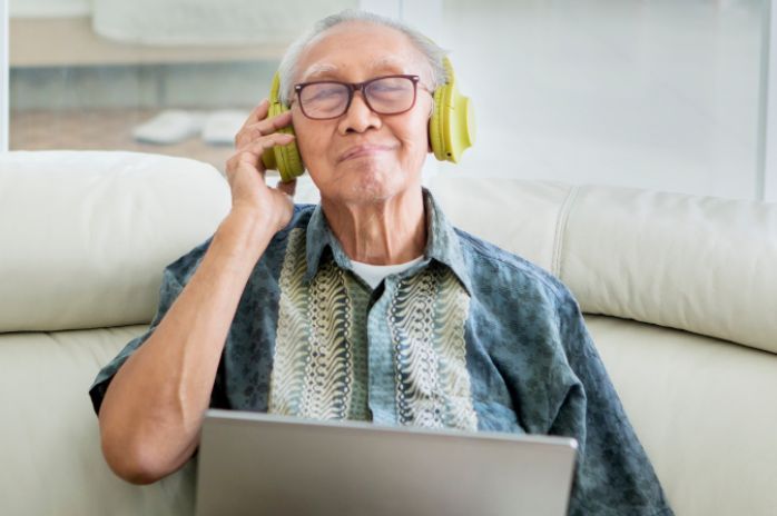 Senior Asian man with headphones on and laptop listening to music relaxing