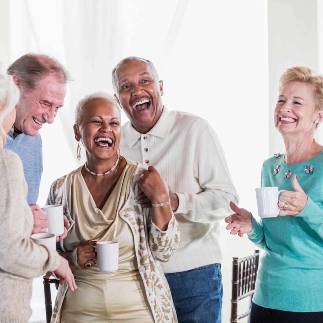 Group of diverse seniors laughing and holding coffee mugs