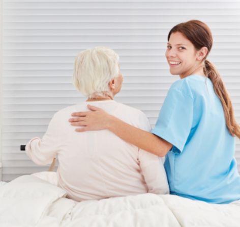 Senior woman sitting on bed with female nurse with nursing and rehab services