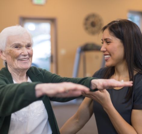 Senior woman with her arms out getting help from female physical therapist