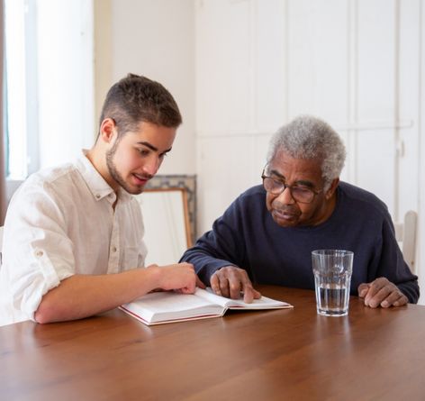 Young man helping senior African American man read