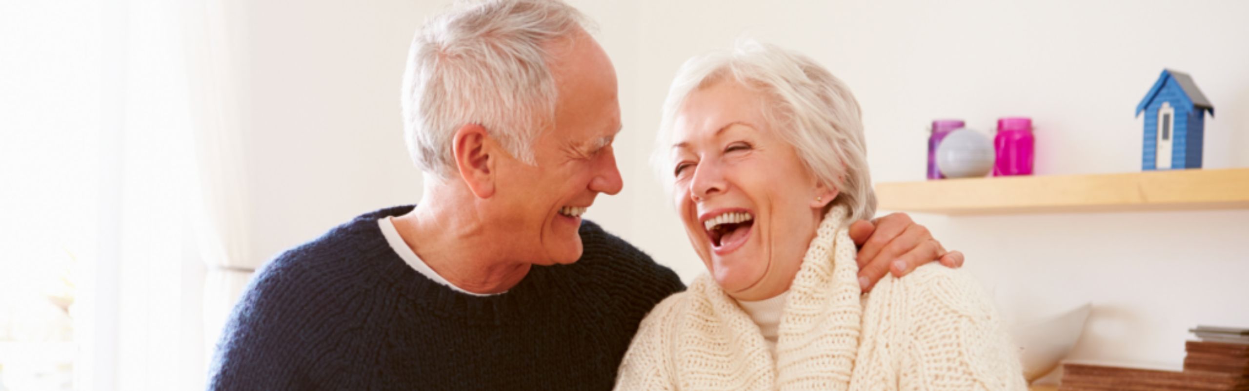 senior couple with man's arm around woman laughing in apartment homes
