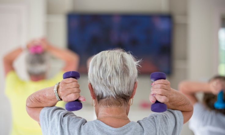 Back of senior woman's head who is lifting purple weights in an exercise class