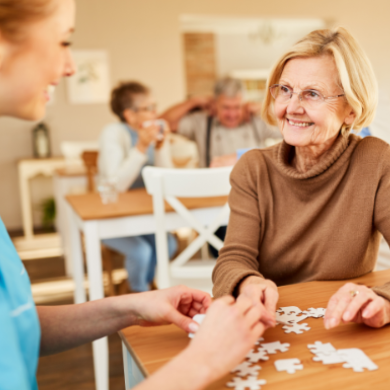 senior woman in memory support completing a puzzle with nurse and smiling