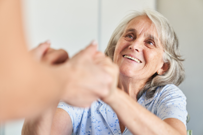 Senior woman in wheelchair looking up at caregiver smiling and holding hands