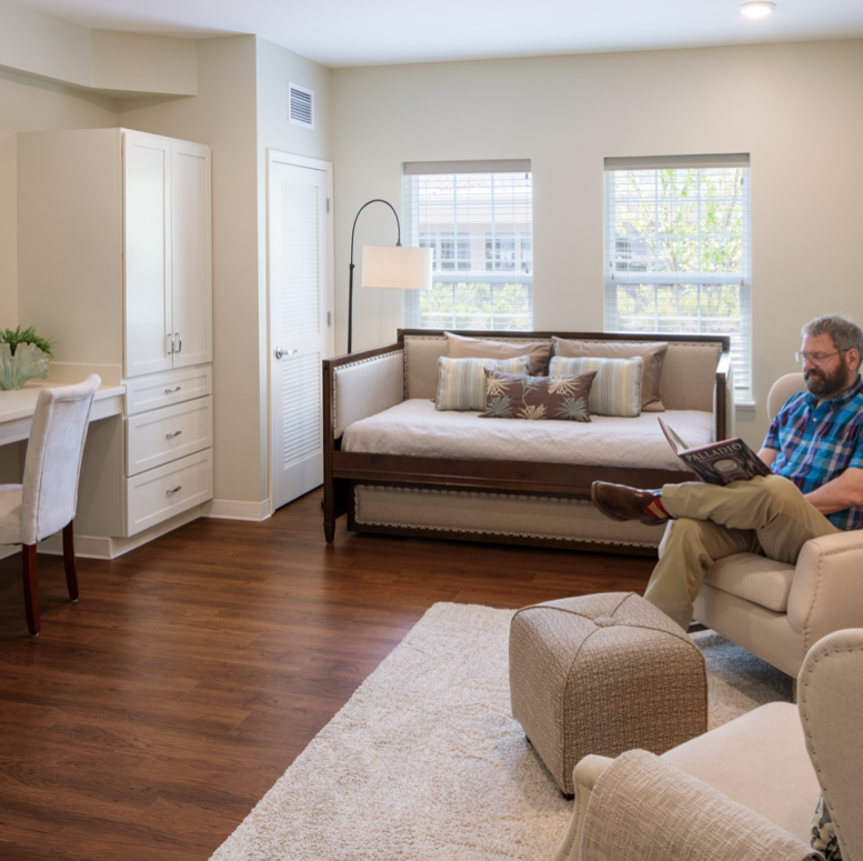 Interior of Wesley Woods memory care apartment with middle aged man sitting in chair reading