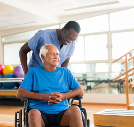 Senior man in wheelchair with male nurse behind him in a rehabilitation gym