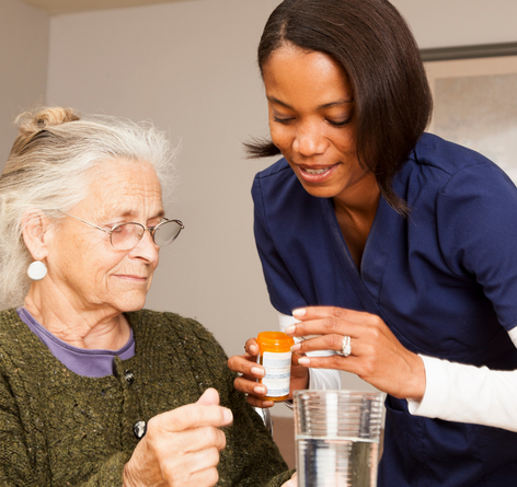 Senior Caucasian woman in glasses receiving medication from female African American caregiver